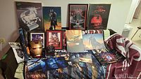 Full view of collection showing Iron Man mask, multiple framed and rolled posters, collectible pins, and Supernatural blanket on couch
