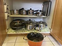 Inside cupboard view showing two shelves with multiple pots, pans, bowls, lids, and cookie sheets.