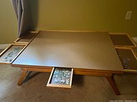 Full front view of the assembled puzzle tray with four extended pull-out drawers containing puzzle pieces around the main board surface.