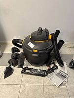 Vacuum body with hose, extension tubes and various attachments arranged on tiled floor