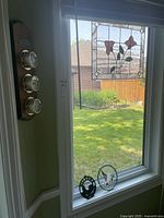 View showing stained glass window panel hanging with floral motif, barometer and round decorative pieces on windowsill and wall-mounted instruments.