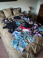 Wide view of multiple ladies swimsuits and sarongs laid out on a bed showing a variety of styles and colors.