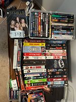 Photo showing various VHS and DVD cases on a table, titles include The Hills VHS, Batman collection DVD, and multiple other movie titles in VHS and DVD form.