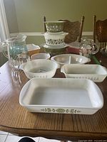 Display of vintage Pyrex and Fire King dishes including casserole dishes with decorative patterns and glass pitchers on wooden table.