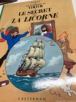 Front cover of 'Le Secret de La Licorne' comic book showing Tintin, Captain Haddock, and a ship illustration inside a circle; text in French.