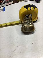 Photo showing the brass twin children bell and measuring tape for size reference on white surface