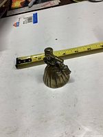 Small brass bell shaped like a woman with a bucket, shown next to tape measure for size reference approximately 3 inches tall.
