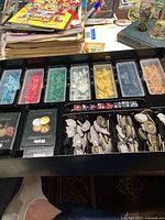 Game components including colored miniature figures, tokens, cards, and dice displayed inside black game box insert with plastic compartments.