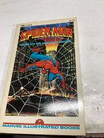 Front cover of Marvel Illustrated Books Spider-Man comic issue 2 showing Spider-Man swinging on webs in a cityscape background.