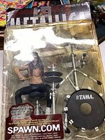 View of unopened Metallica drummer action figure in original packaging showing detailed drum kit and figure.
