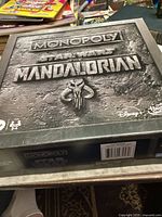 Top of the Monopoly Star Wars The Mandalorian box with embossed text and emblem.