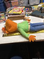 Side view of plush Scooter doll lying horizontally with measuring tape showing approximately 18 inches in length.