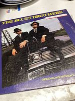 Front cover of The Blues Brothers original soundtrack vinyl record sleeve featuring the characters on a car hood.