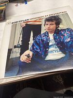 Front cover of 'Highway 61 Revisited' showing Bob Dylan in blue jacket, holding a cigarette.