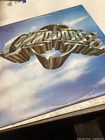 Front cover of The Commodores vinyl record album featuring the band logo on a blue sky background.