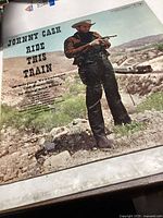 Front cover of Johnny Cash Ride This Train Columbia record showing Johnny Cash in cowboy clothes holding a rifle against a desert background.