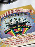 Colorful Magical Mystery Tour album cover featuring Beatles members in white animal costumes on rainbow background with psychedelic title text. Also shows part of the 24-page picture book the lot includes.
