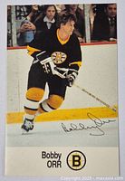 Front view of Bobby Orr hockey card in Boston Bruins black and yellow uniform skating on ice with Sher-Wood stick and printed signature.