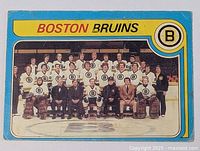 Boston Bruins vintage team photo card with players and staff on ice rink background, blue border, yellow header, and Bruins logo.