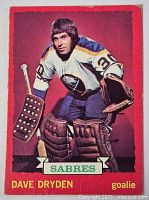 Front of vintage Dave Dryden Buffalo Sabres hockey card showing player in full goalie uniform, colorful red background.