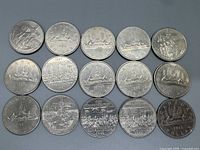 Top view of the reverse sides of 15 Canadian silver dollar coins showing canoes, commemorative 1967 Confederation designs, and other historic scenes.