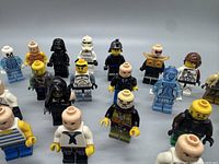 Photo showing a front angled view of 23 LEGO minifigures arranged in rows on a white surface, highlighting worn surfaces and variety in character design.