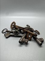 Photo showing a pile of 7 early vintage skeleton keys with various designs and worn, rusted metal surfaces.