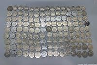 Top-down view of all 135 Canadian nickels laid out in rows on a grey surface, showing the reverse with the beaver design on most coins.