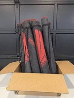 Box containing multiple rolled 3x5 Adirondack style indoor/outdoor rugs with red maple leaf print tightly secured with black straps.