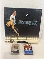 Bruce Springsteen & The E Street Band Live 1975-85 boxed 3 cassette set with visible wear on cover, plus two other cassette tapes (Led Zeppelin and MCA compilation) on white background.