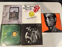 Top view showing five vintage rock LP covers arranged on table including Led Zeppelin IV, Rolling Stones 'Miss You' and 'Tattoo You', Alice Cooper and Rolling Stones group photo album.