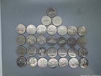 Top view of 31 Canadian silver dollars arranged in a pyramid, showing various designs on the reverse including canoes, flowers, and buildings.