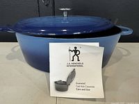 Blue gradient oval enameled cast iron Dutch oven with lid and care manual booklet in front.