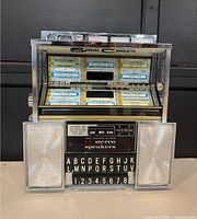 Front view of Seeburg Stereo Consolette showing coin slot, illuminated title cards, letter-number selectors, and built-in speakers.
