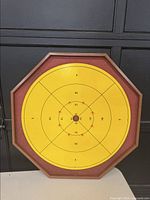 Octagonal wooden crokinole board side showing yellow playing surface with scoring zones and central hole.