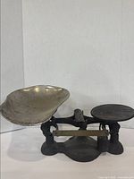 Front view of vintage cast iron candy scale showing large metal tray, flat plate, balance beam with brass scale, and cast iron base.