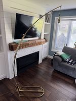 Full view of vintage brass arc lamp showing large curved arm, oval base, positioned in living room near fireplace and TV.