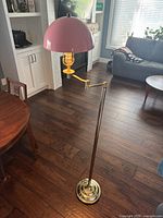 Full view of vintage brass floor lamp with pink dome shade standing on wood floor in living room setting