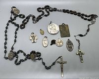 Full view of the lot showing two wooden beaded rosaries and various religious medals spread out on a white surface.