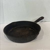 Angled side view of black cast iron fry pan showing handle and worn cooking surface.