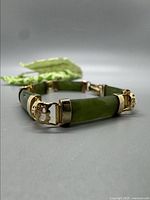 Close-up of green jade segments with shiny gold-tone floral connectors and clasp of the vintage bracelet.