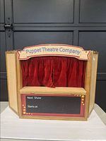 Front view of vintage wooden finger puppet theatre with red velvet curtain closed and signage