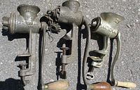 Three antique metal meat grinders clamped side-by-side, all with wooden crank handles and heavy metal construction.
