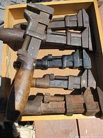 Top view of six wrenches in wooden box with wooden handles and weathered metal, showing screws and jaws for pipe wrench function.