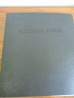 Closed black binder with textured cover and embossed label.