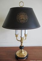 Front view of vintage brass and marble Bouillotte style desk lamp with Ohio University crest on black parchment shade, showing three faux white candlesticks and solid brass and marble base.