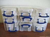 Nine clear plastic drawer containers stacked in three columns, each with blue locking handles