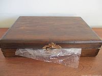Closed wooden box with a clasp and plastic protective wrap beneath the clasp