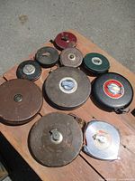 Lot of 11 vintage measuring tapes of varying sizes and materials displayed on wood.