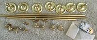 Photo showing six brass drawer pulls with round backplates, several brass curtain rods, and scattered drawer knobs laid out on carpeted floor to display elements.